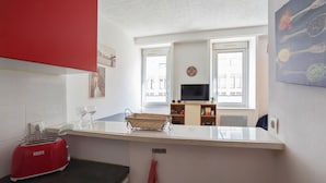 A compact kitchen with a red toaster, a small sink, and a window with a view of buildings.