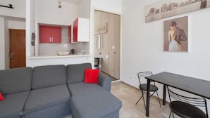 A modern living room with a grey sectional sofa, a dining table with chairs, and a kitchen area with red cabinets.
