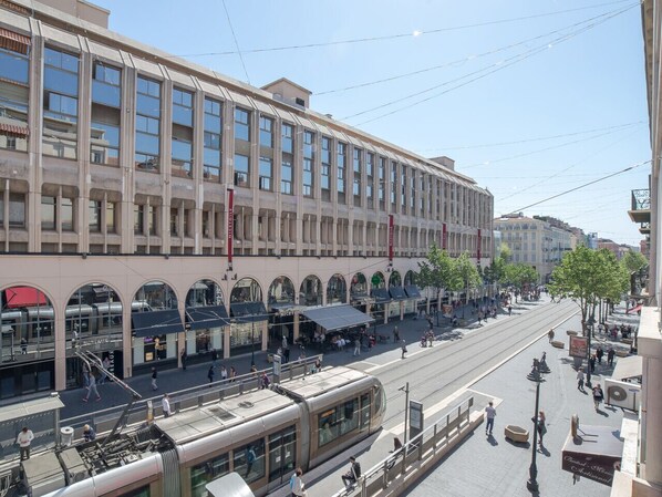 A modern building with a large glass facade, multiple levels, and a tram line running in front. - Studio Promenade - Welkeys (Nice)