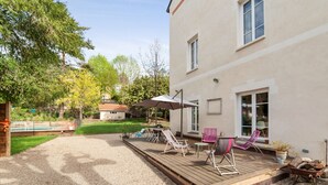 Eine überdachte Terrasse mit Holzdeck, Gartenmöbeln und einem Schwimmbad im Hintergrund.