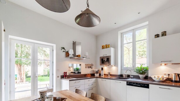 Eine moderne Küche mit weißen Schränken, einem Holzespeisetisch und einem großen Fenster, das für natürliches Licht sorgt.