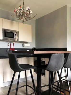 Uma cozinha moderna com micro-ondas, lustre e dois banquetas pretas.
