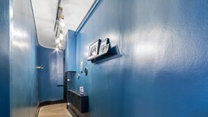 A hallway with blue walls, wooden flooring, a black shelf with framed photos, and a light fixture. - Appartement Majorel - Welkeys (Lyon)