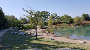 A lakeside area with white lounge chairs and a small building, likely a cabin or hut, near the water. - Comfortable 3 bedroom mobile home with air conditioning in Provence - Swimming pool and private lake (La Roque-d'Anthéron)