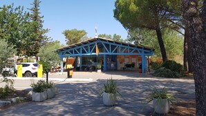 A blue-roofed building with a reception area, potted plants, and a white car parked outside. - Comfortable 3 bedroom mobile home with air conditioning in Provence - Swimming pool and private lake (La Roque-d'Anthéron)