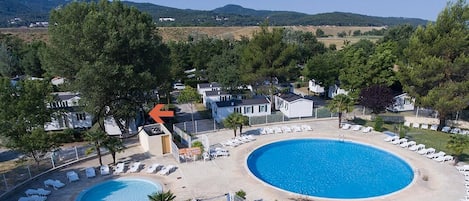 A resort with two swimming pools, lounge chairs, and villas surrounded by trees.
