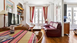 Un salon avec un plancher en bois, un canapé, un téléviseur et une bibliothèque.