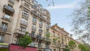 Une vue de rue avec une rangée de bâtiments, dont un restaurant avec un auvent rouge et une enseigne indiquant « Bistro ». Des voitures sont garées le long de la rue et une moto est stationnée sur le trottoir.