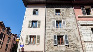 A multi-story building with stone facade, multiple windows with shutters, and a visible street sign.