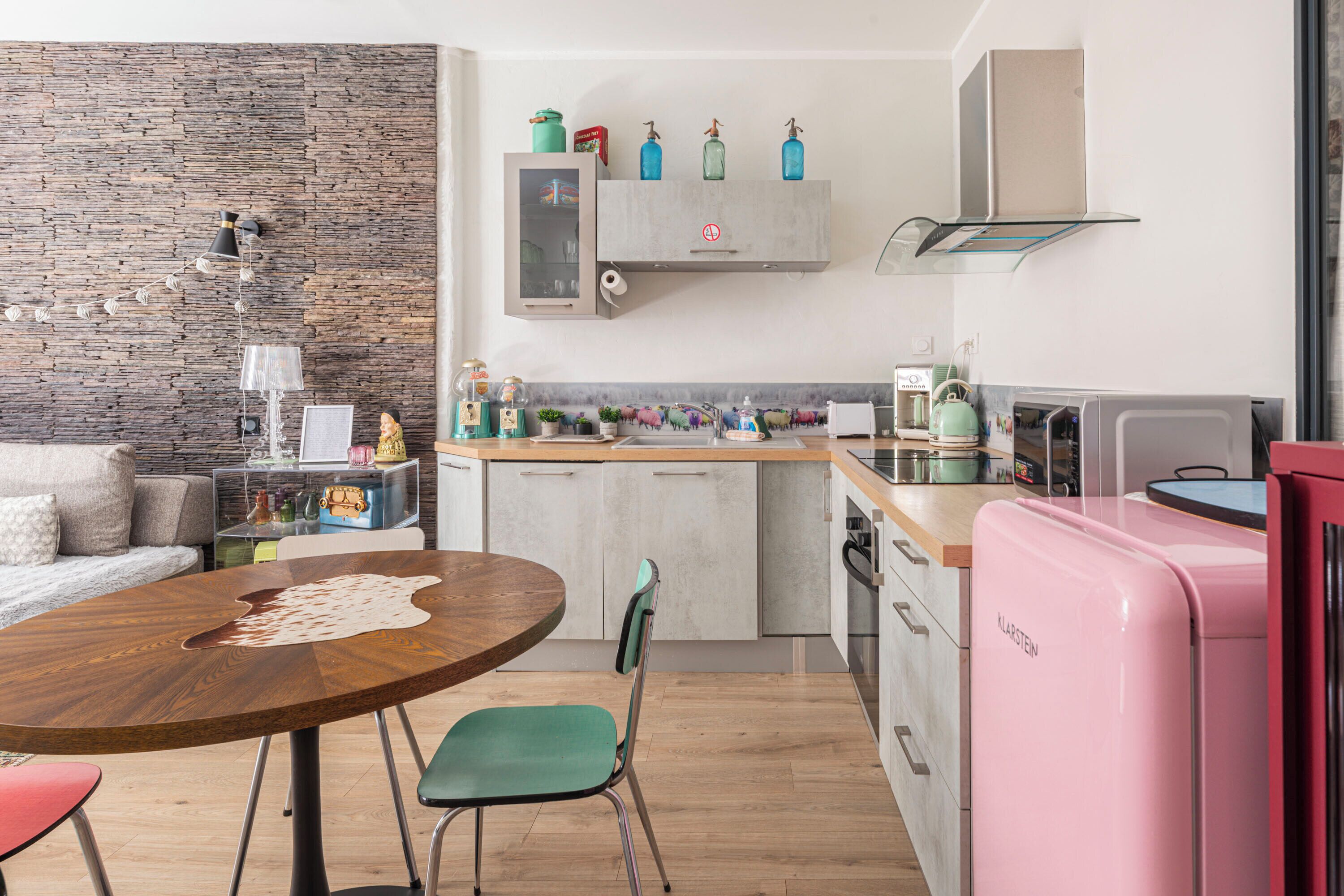 A modern kitchen with a stone wall, a wooden dining table, and a pink refrigerator.