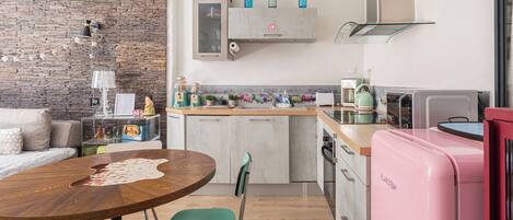 A modern kitchen with a stone wall, a wooden dining table, and a pink refrigerator.