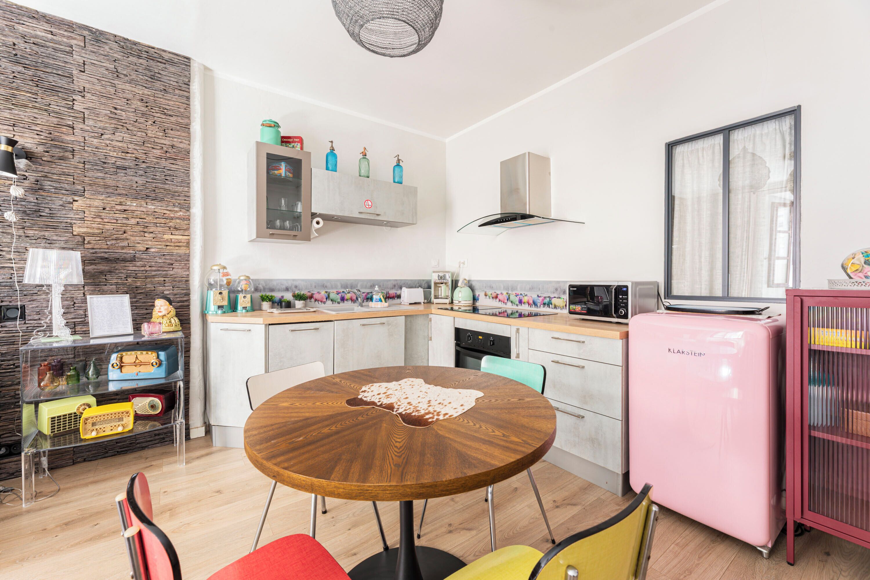 A modern kitchen with a round wooden table, white cabinets, a pink refrigerator, and a decorative wall.