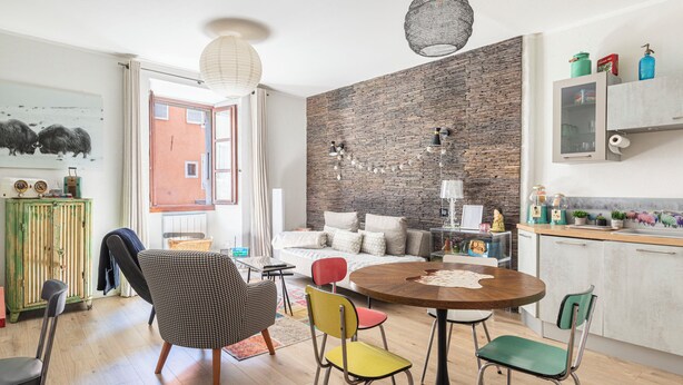 A modern kitchen with a dining area, a brick wall, and a view through an open door.