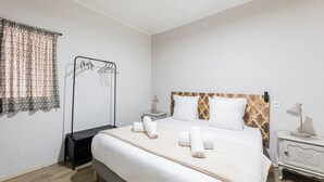 A bedroom with a bed, bedside tables, a hanging clothes rack, and a window with curtains.