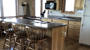 Een keuken met houten kastjes, een groot eiland met barstoelen, een koelkast en een magnetron.