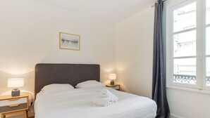 A neatly made bed with white linens and towels, a bedside table with a lamp, and a window with a view of buildings. - Appartement du Marché St Honoré - Welkeys (Paris)