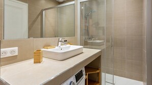A modern bathroom with a glass shower enclosure, a white sink, and a wooden storage unit. - Appartement du Marché St Honoré - Welkeys (Paris)