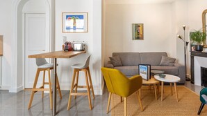 A modern living room with a grey sofa, a small round table, and a yellow chair. There is a kitchen area with a wooden table and stools. - Appartement du Marché St Honoré - Welkeys (Paris)