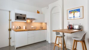A modern kitchen with white cabinets, a stainless steel oven, a wooden countertop, and a small dining area with stools. - Appartement du Marché St Honoré - Welkeys (Paris)