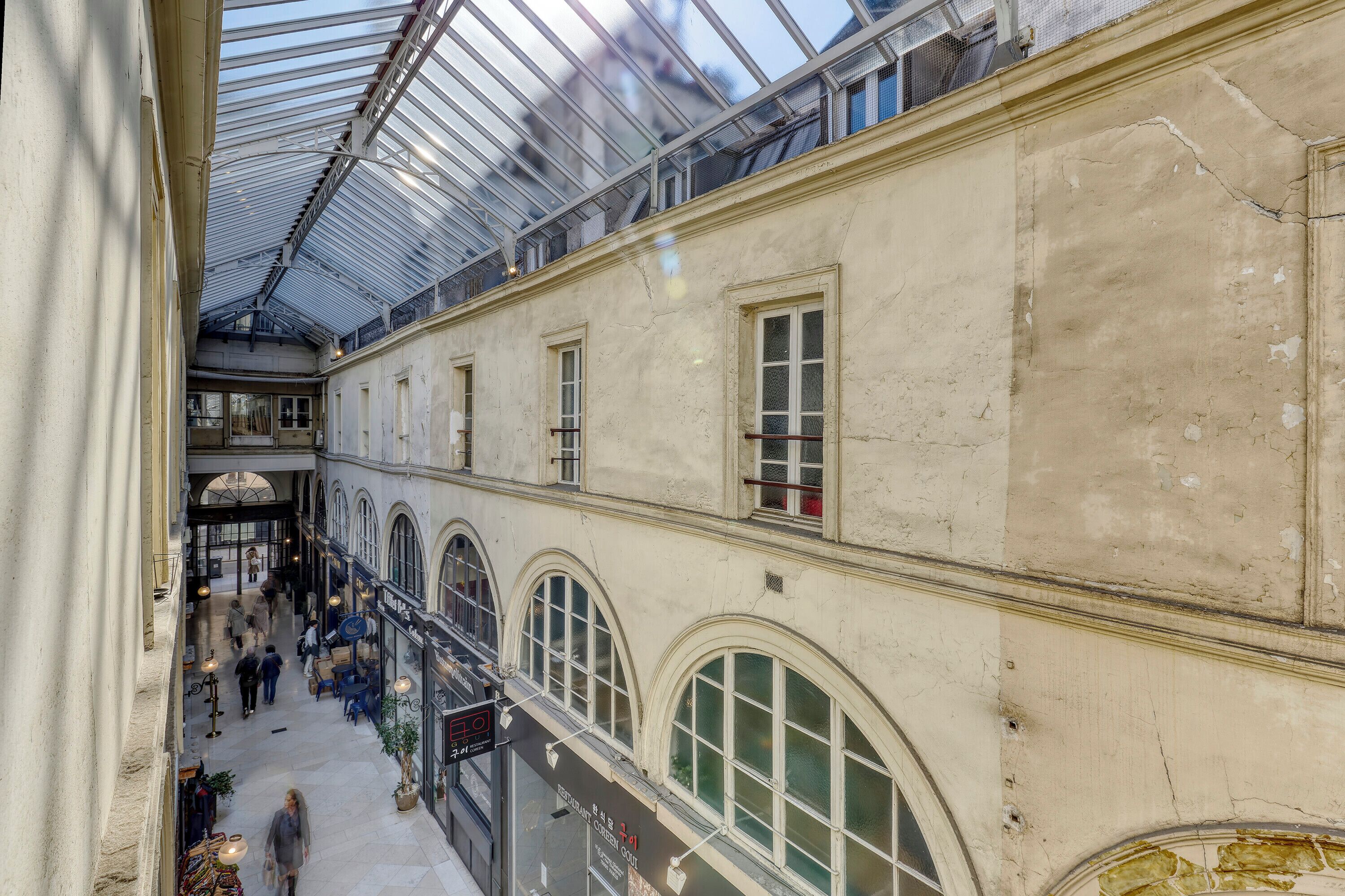 An interior view of a building with arched windows and a glass ceiling, featuring a central walkway and multiple levels.