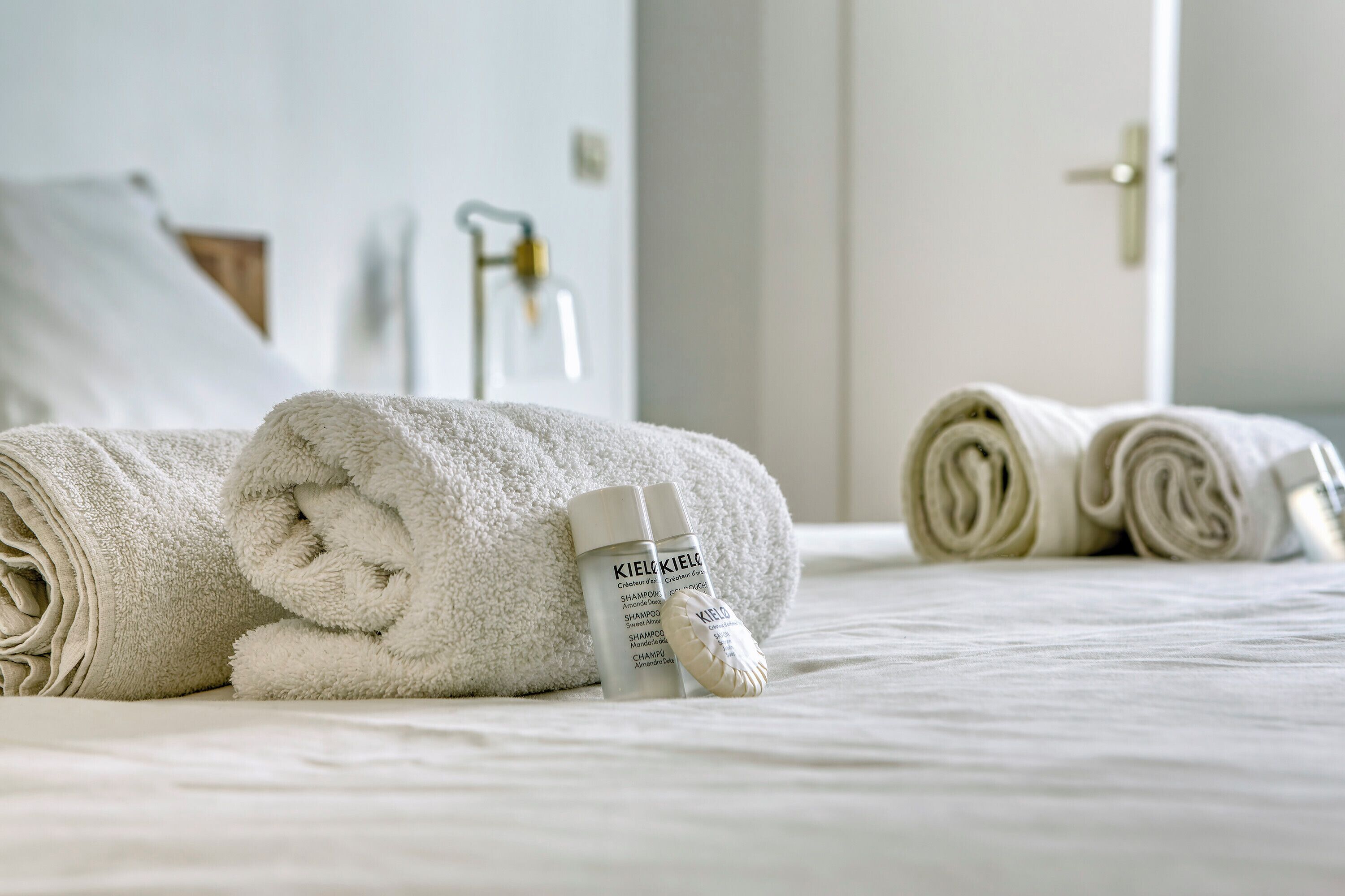 Cama bem arrumada com toalhas brancas dobradas e um frasco de shampoo.