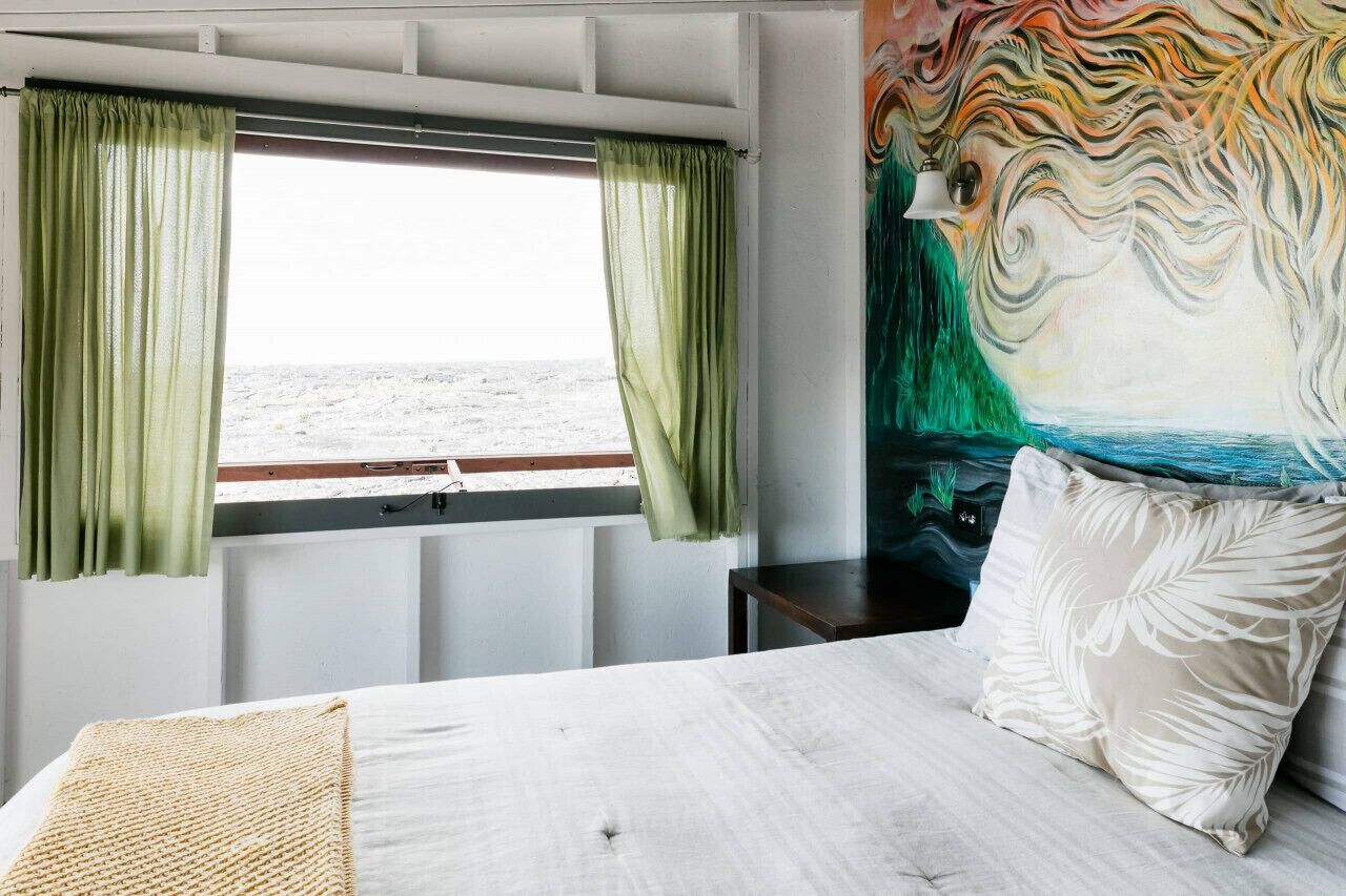 A room with a bed, a window with curtains, a painting, and a nightstand.