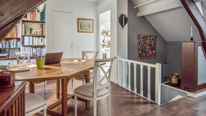 Un acogedor espacio tipo loft con una mesa de comedor de madera, sillas blancas y una estantería llena de libros.