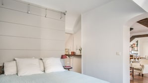Un dormitorio con una cama grande, una mesita de noche con lámpara y una estantería al fondo.