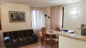 Una sala de estar con sofá, mesa de comedor, sillas y una pequeña cocina con mostrador y ventana.