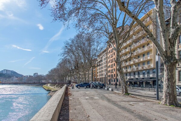 Une promenade le long de la rivière, bordée de voitures garées, d’arbres et d’immeubles à plusieurs étages dotés de balcons.
