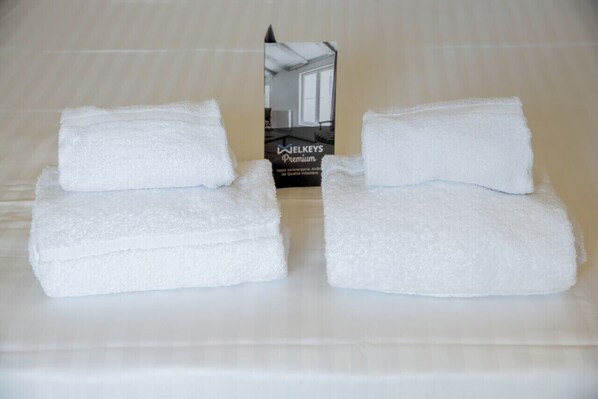 Neatly folded white towels stacked on a bed with a visible box labeled "JELKEYS Premium" in the background.