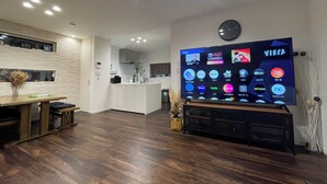 A modern kitchen with a dining area, a TV displaying various apps, and a clock on the wall.