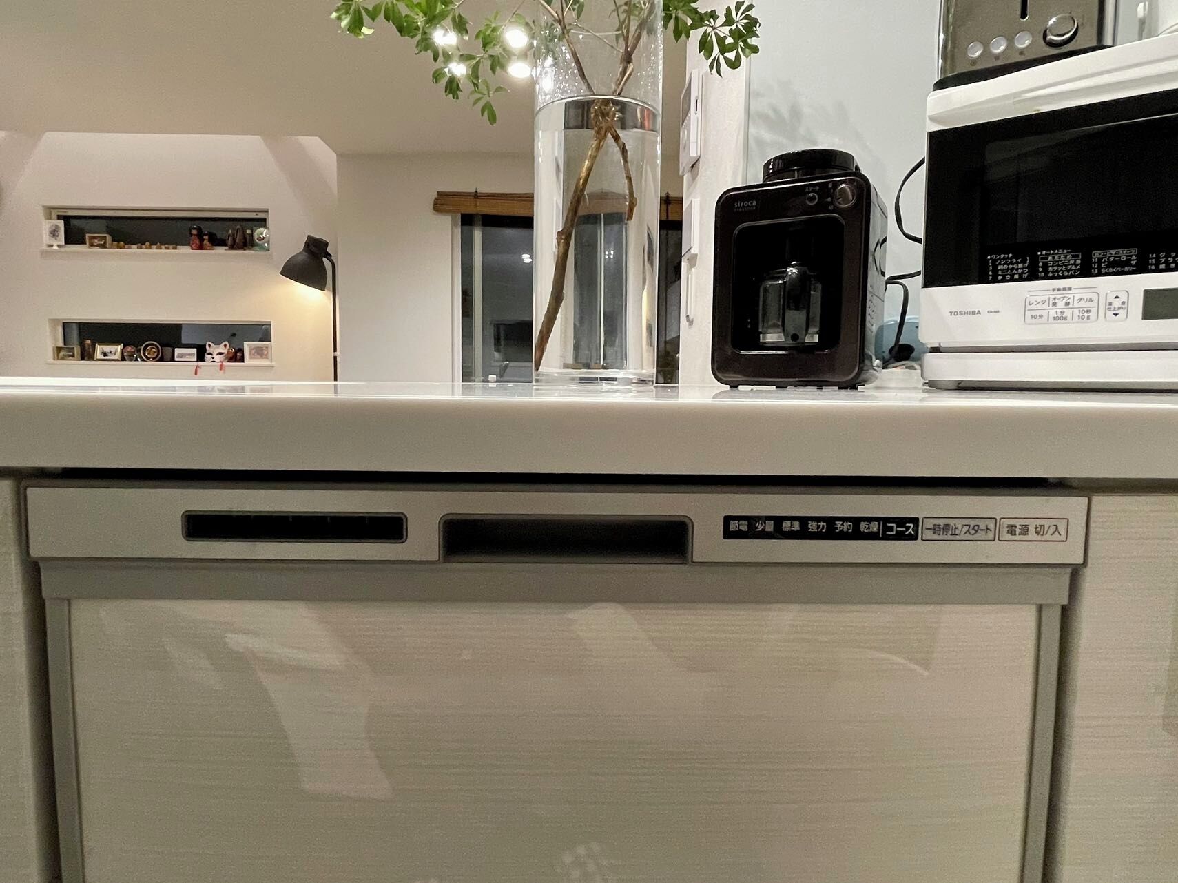 A kitchen counter with a coffee maker, microwave, and a vase with branches.