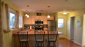 A kitchen with wooden cabinets, stainless steel appliances, and a bar area with three stools. - Light and bright family-friendly cottage (Portland)