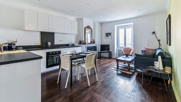 A modern kitchen with white cabinets, a dining area with a table and chairs, and a living space with a sofa and a coffee table. - Appartement Tromba - Welkeys (Lyon)