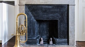A fireplace with a black mantle, a brass trombone, and two busts on the mantel. - Appartement Tromba - Welkeys (Lyon)