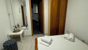 Quarto com cama, mesa de cabeceira, espelho, guarda-roupa e banheiro visível por uma porta aberta.