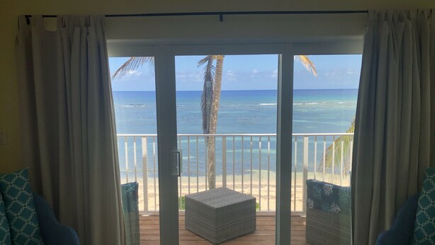 Quarto com vista para o oceano através de uma porta de correr de vidro, com varanda e mobiliário de vime, além de um tapete estampado.
