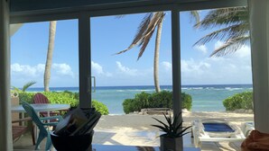 Vista de um quarto com porta de vidro para a praia, mostrando uma mesa com uma planta, uma revista e uma cadeira.