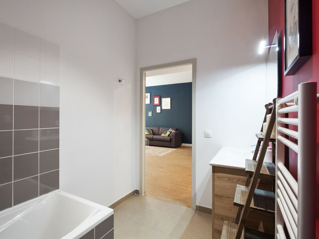 A modern bathroom with a bathtub, a wooden ladder, and a red wall.