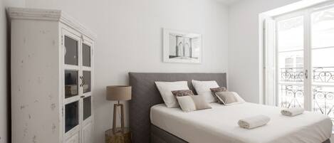 A bedroom with a large bed, a wardrobe, a lamp, and a window with a view.
