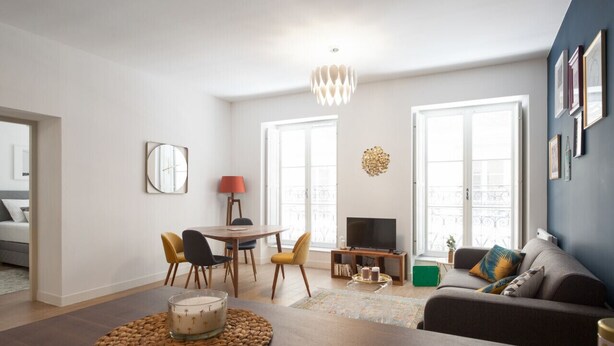 Ein modernes Wohnzimmer mit Essbereich, einer Couch, einem Fernseher und einem Kronleuchter.