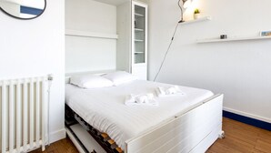 Ein Schlafzimmer mit einem Bett, einem weißen Heizkörper, einem hängenden Spiegel und einem Regal mit einer Lampe und Kleinigkeiten.