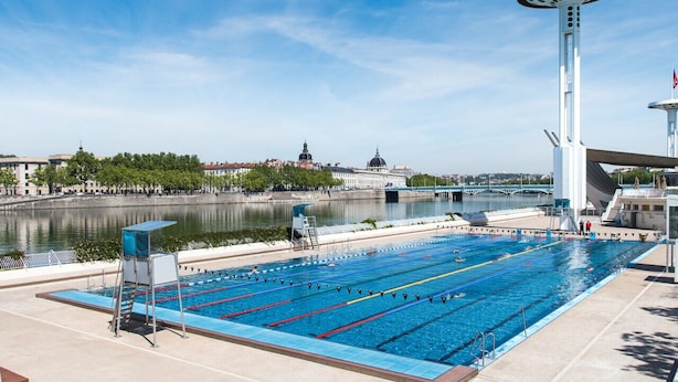 Une piscine avec des couloirs de nage, un plongeoir et une haute structure en forme de tour surmontée d’un drapeau.