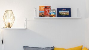 Un mur blanc orné d’une étagère où sont rangés des livres de voyage et d’un luminaire au design géométrique.