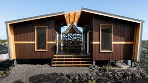 A wooden cabin with a sloped roof, a central entrance with steps, and a view of the surrounding landscape. - Volcano Escape  Epic Tiny Home on Lava Field with Volcano Views (Pāhoa)