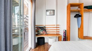 A bedroom with a wooden bench, a small table, a wall-mounted shelf, and a window with curtains. - Volcano Escape  Epic Tiny Home on Lava Field with Volcano Views (Pāhoa)