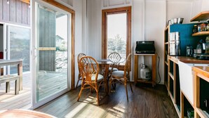 A cozy kitchen with a wooden ceiling, a dining table with chairs, and a view through a glass door to an outdoor deck. - Volcano Escape  Epic Tiny Home on Lava Field with Volcano Views (Pāhoa)