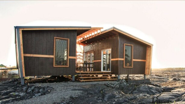A wooden cabin with a porch, large windows, and a gravel ground. - Volcano Escape  Epic Tiny Home on Lava Field with Volcano Views (Pāhoa)