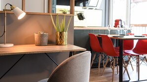 Ein moderner Essbereich mit Holztisch, roten Stühlen, einem Schreibtisch mit Lampe und einem Blumentopf.